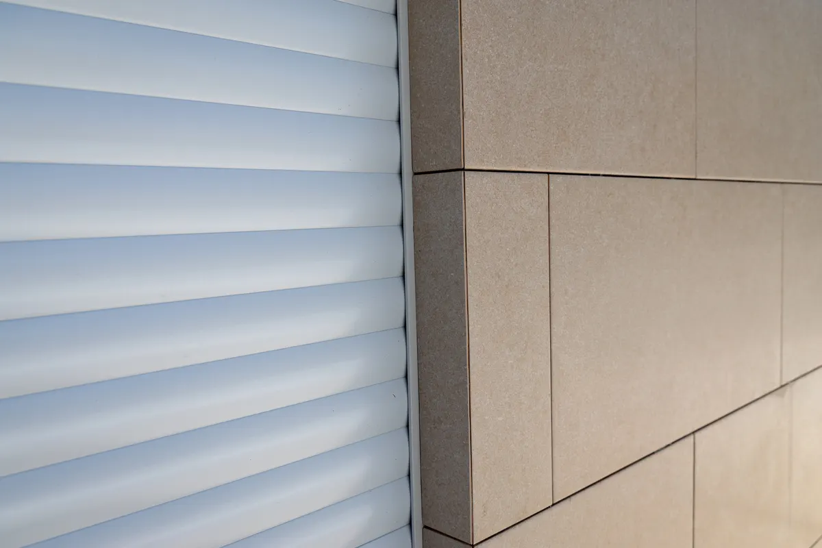 Détail rapproché des lames d'un volet roulant blanc le long de la coulisse, façade en pierre